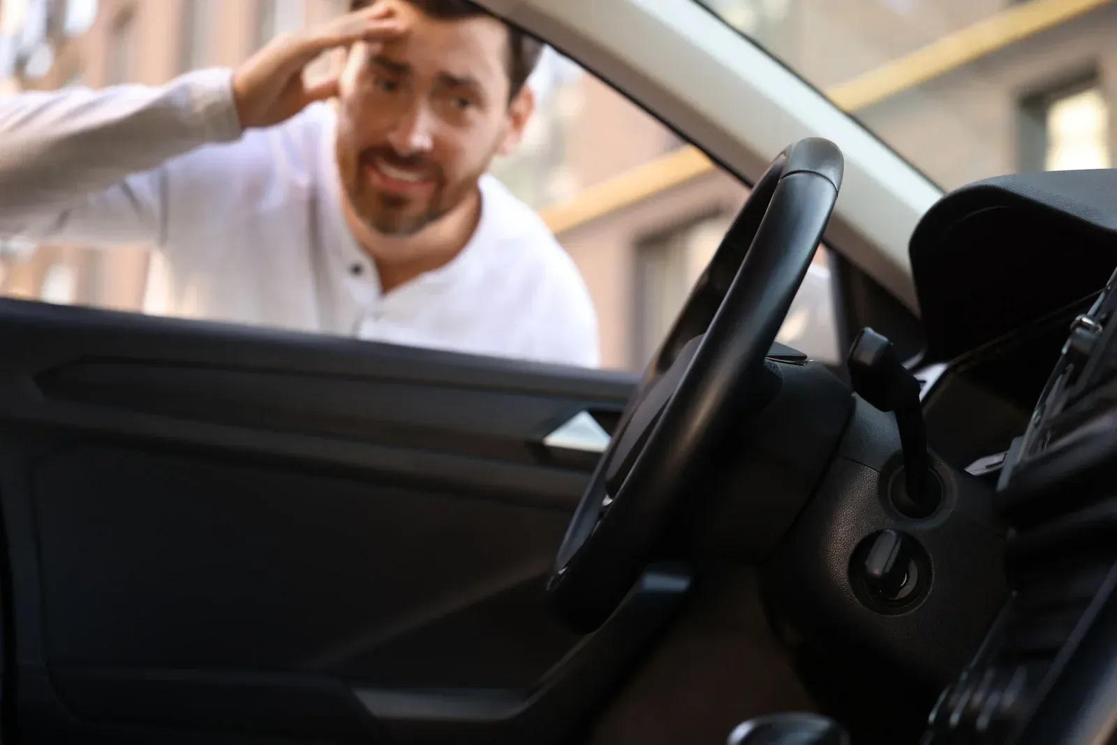 Man locked out of car, hand on forehead, looking inside.
