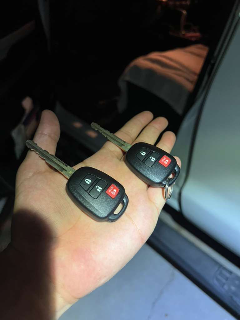 Two car key fobs held in a hand inside a vehicle, one with a red panic button.