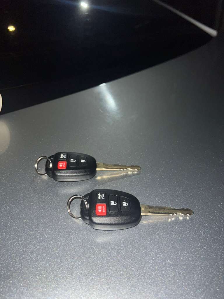 Two black car key fobs with silver keys on a gray surface.