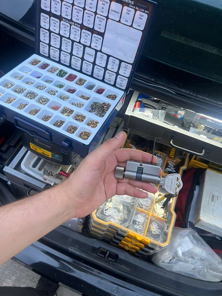 Hand holding small gray electronic parts beside an open toolbox with organized drill bit and bit sets