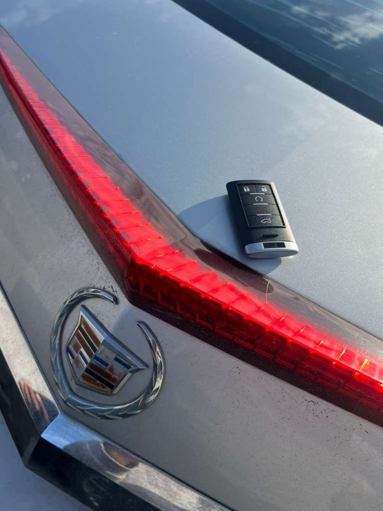 Close-up of a silver Cadillac trunk with red taillight strip and key fob resting on top.