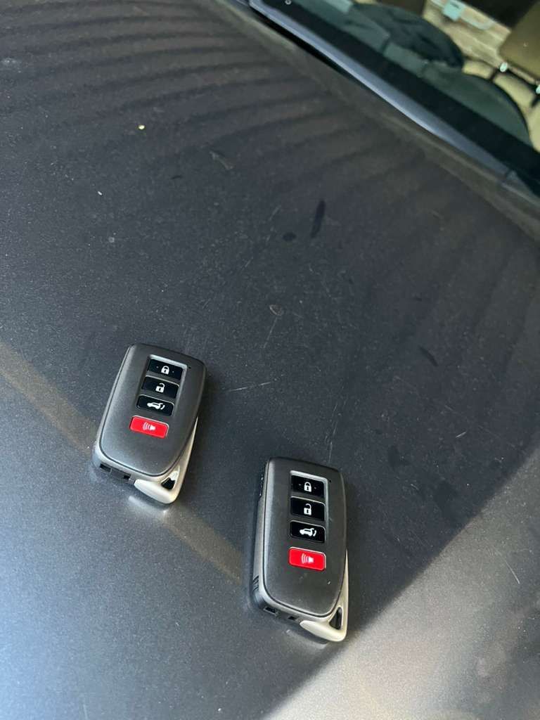 Two black car key fobs on a dark textured surface.