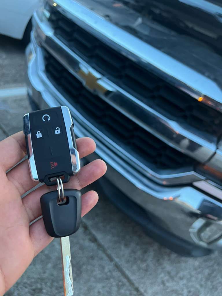 Hand holding a black car key fob in front of a silver Chevrolet grille