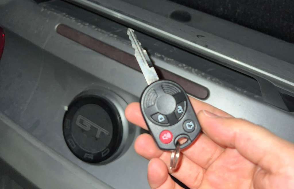 Hand holding a car key fob beside a vehicle door lock and handle