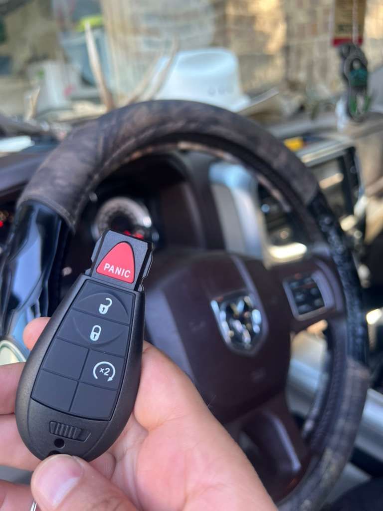 Hand holding a black Dodge car key fob inside a vehicle, with the steering wheel in view.