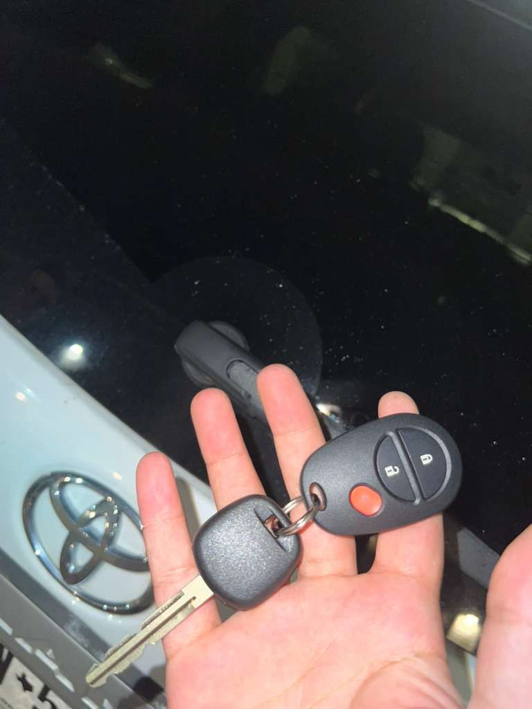 Hand holding a Toyota car key fob and metal key near a white Toyota emblem