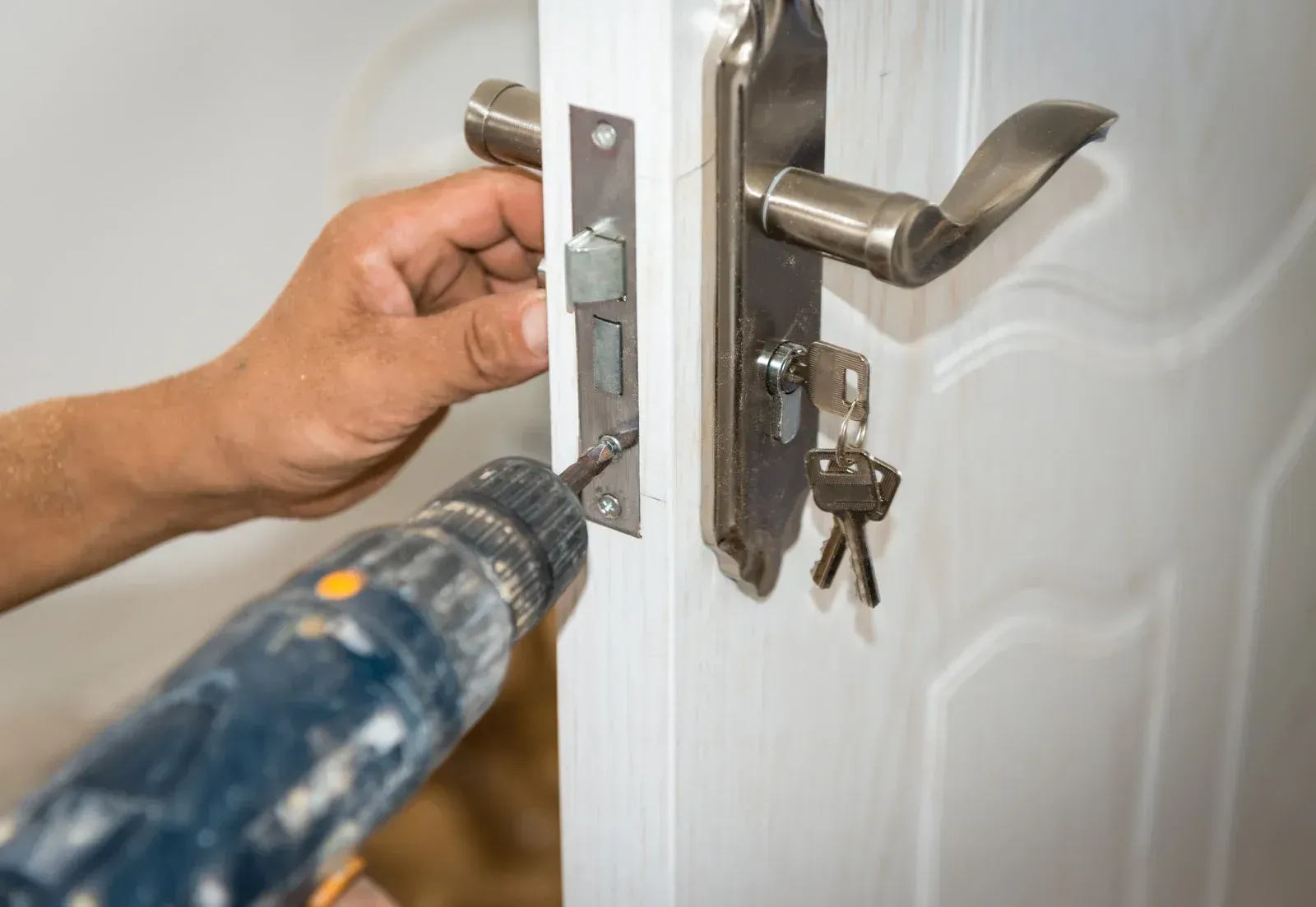 Person using a power drill to install a door lock on a white door.