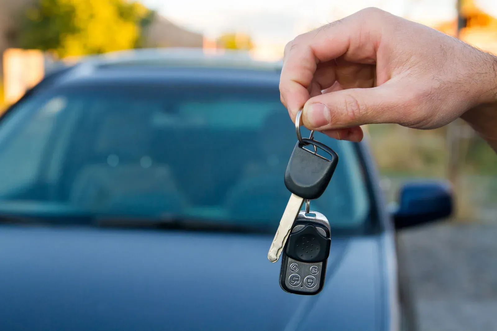 Hand holding car keys in front of a blue car outdoors