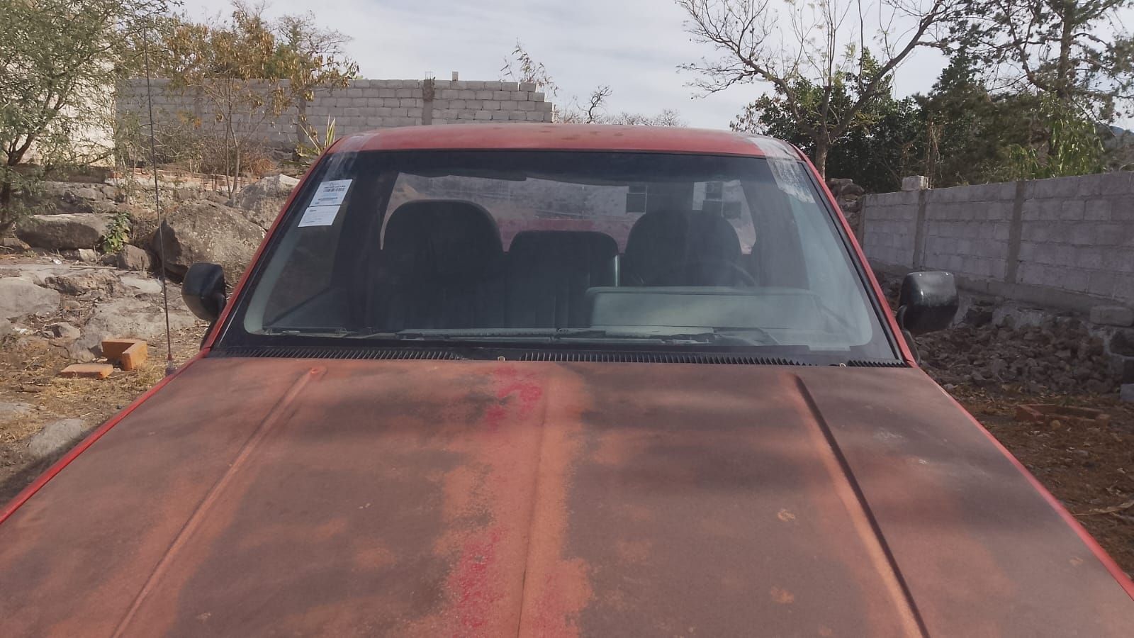 Un coche rojo oxidado está aparcado en un campo de tierra.