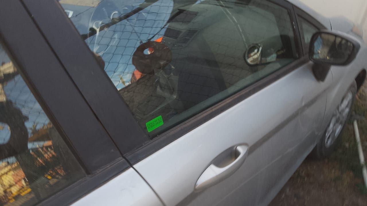 Un coche plateado está aparcado delante de una valla de alambre.