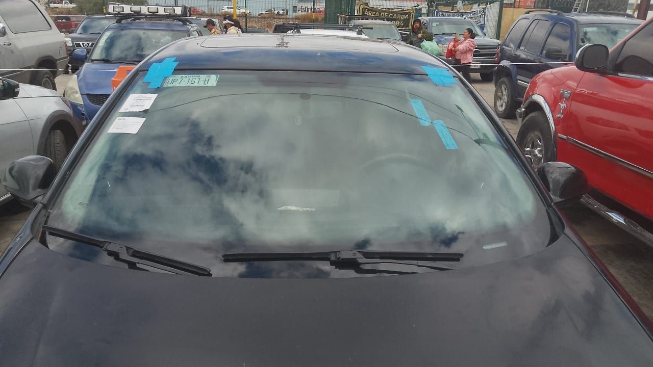 Un coche negro está aparcado en un estacionamiento con otros coches.