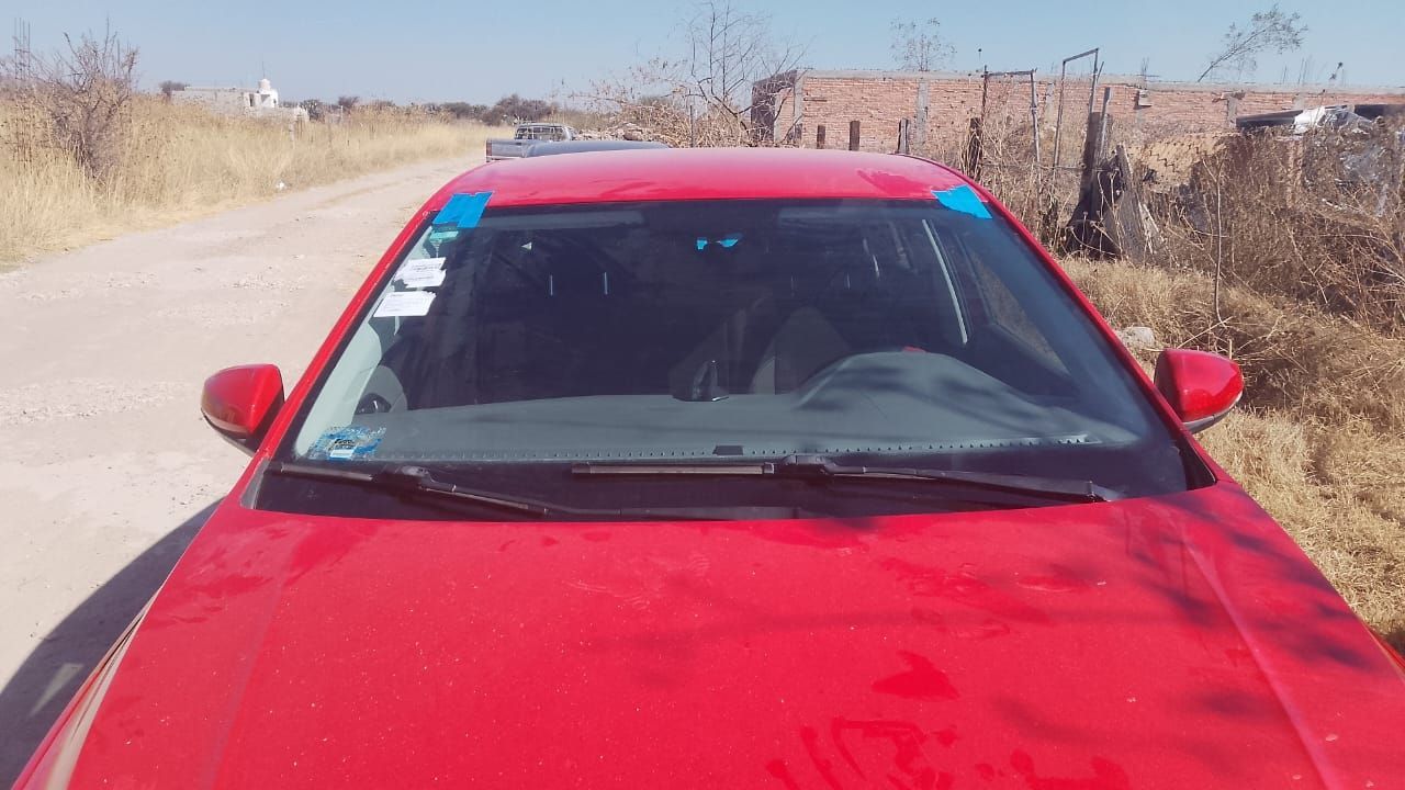 Un coche rojo está aparcado al costado de un camino de tierra.