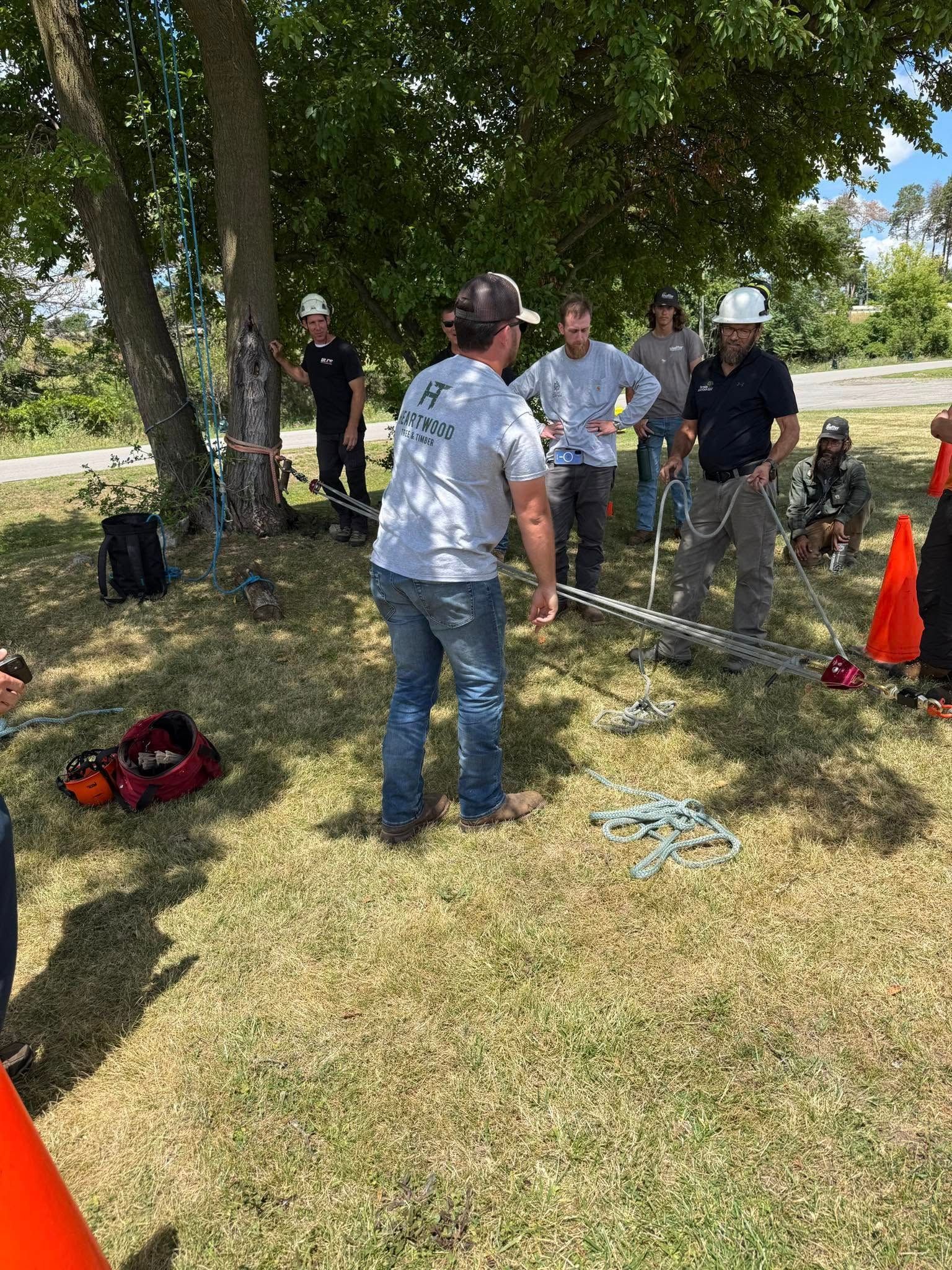 A group of people watch a man demonstrate equipment under a tree.