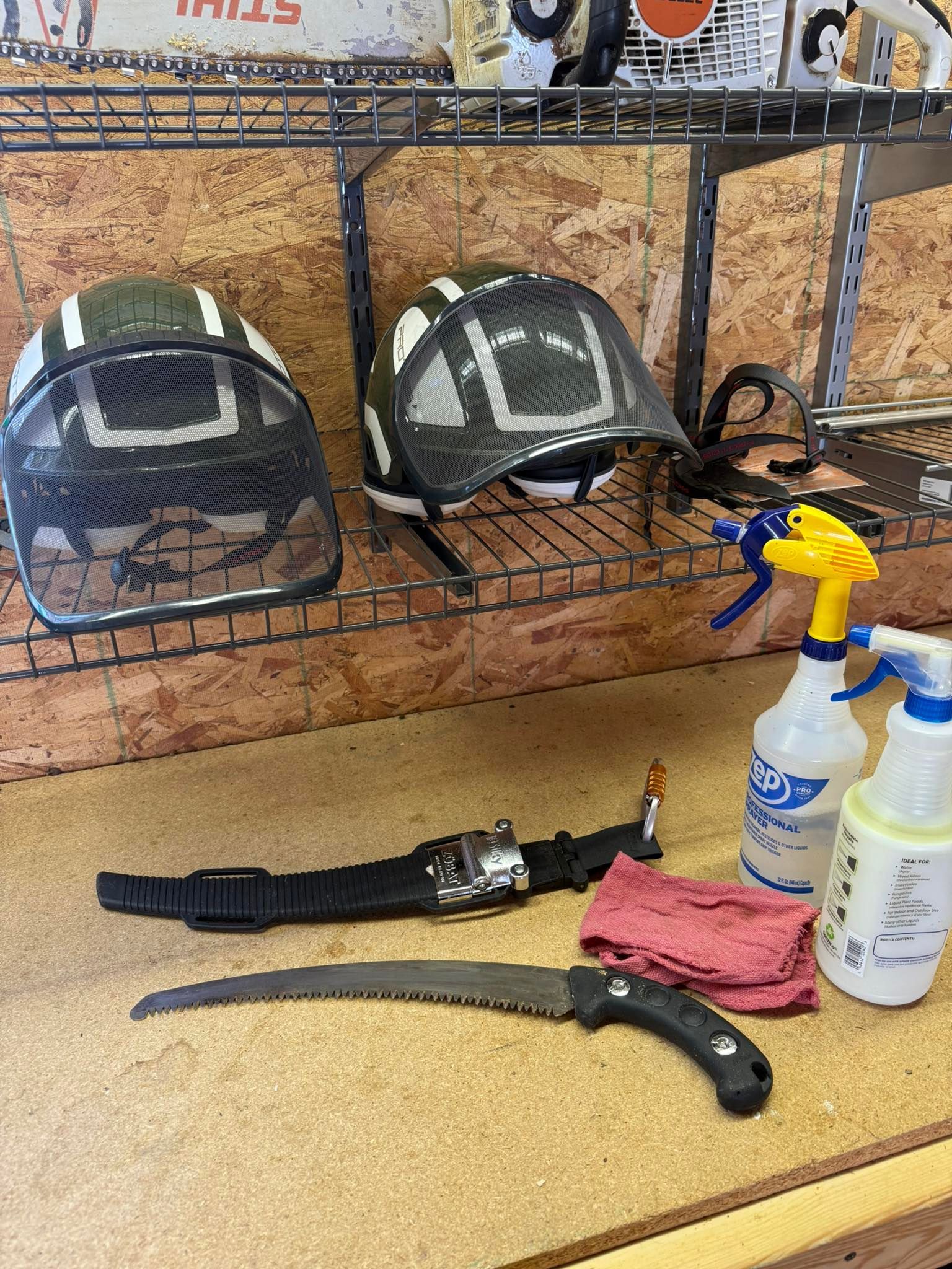 Two safety helmets, saw, belt, spray bottles, and a rag on a workbench.