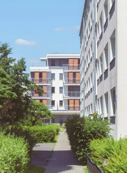 Pathway between apartment buildings with green bushes, blue sky.