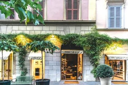 Storefront with a stone facade, gold doors, and climbing vines, framed by trees and awnings.