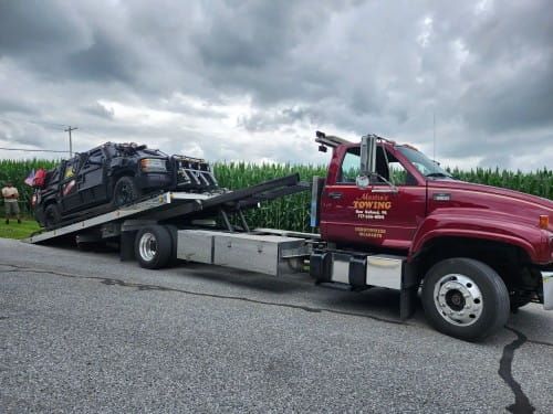 Martin's tow truck loading a black vehicle on a flatbed by a roadside under cloudy skies