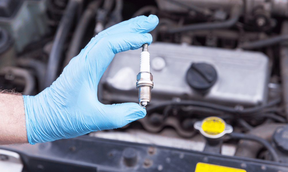 Technician holding spark plug for replacement near engine