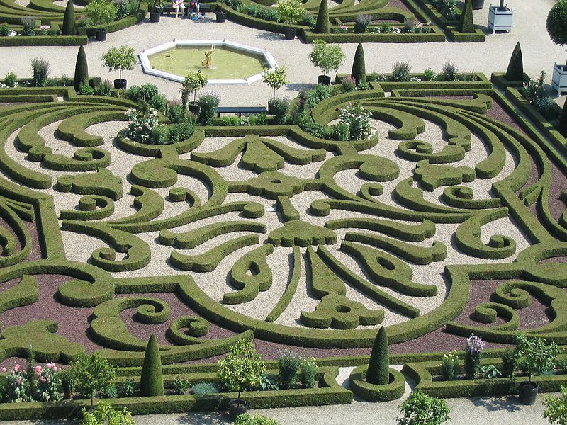 Een formeel tuinlabyrint met keurig gesnoeide groene hagen en een geometrisch patroon in het midden.