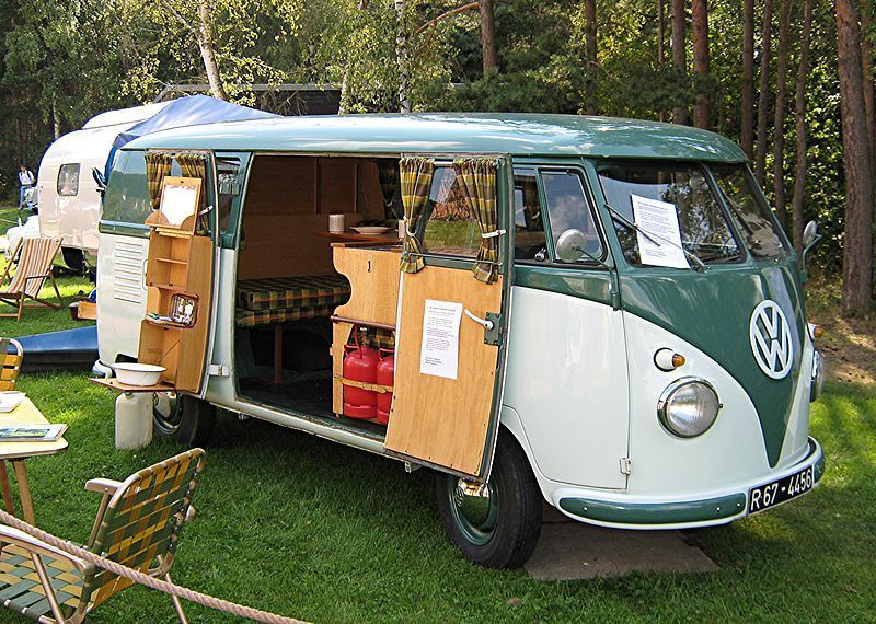 Een vintage Volkswagenbusje met open zijdeuren, geparkeerd in de buitenlucht op een camping.