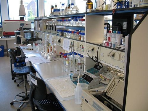 Laboratoriumtafel met glaswerk, instrumenten en computerapparatuur in een licht onderzoekslaboratorium.