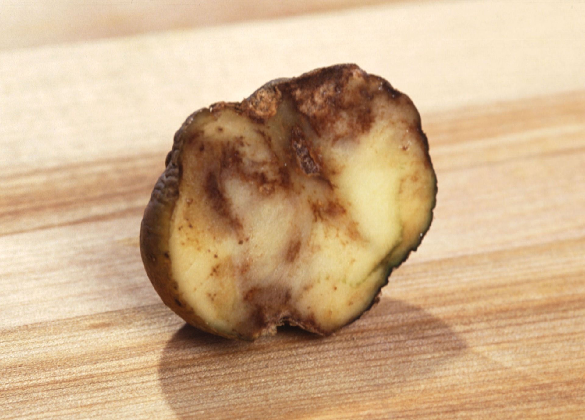 Snijd een aardappel met een bruine schil dwars doormidden op een houten snijplank.
