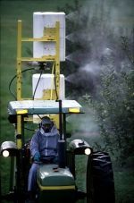 Een persoon die op een groene tractor rijdt, sproeit nevel in een bosrijk veld.
