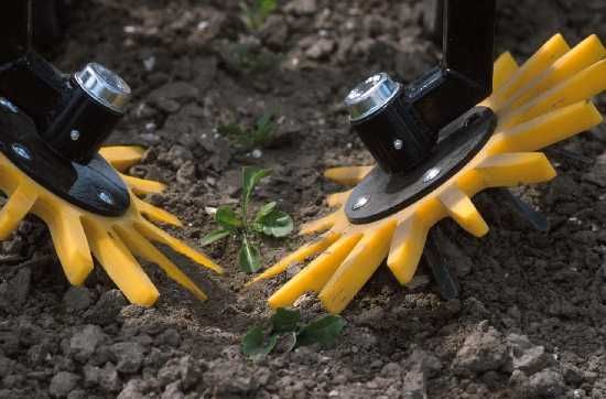 Twee gele tuingereedschappen die in de grond graven, met zwarte handvatten en een klein groen uitsteeksel ertussen.