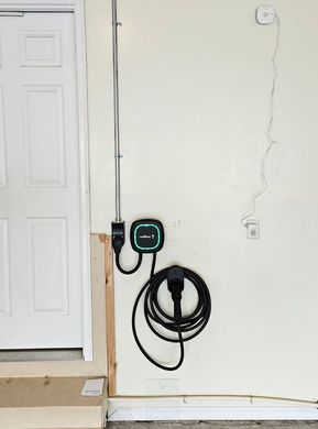 Wall-mounted EV charger with coiled cable beside a white door in a room