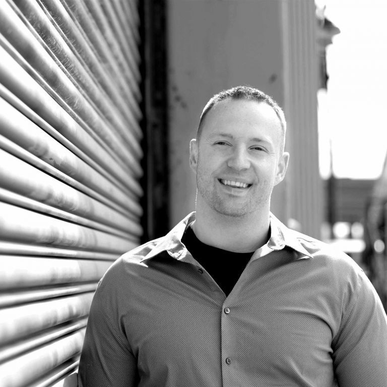 Smiling person standing beside a metal shutter in black-and-white photo