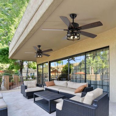 Covered patio with wicker seating, black coffee table, and ceiling fans beside large sliding glass doors