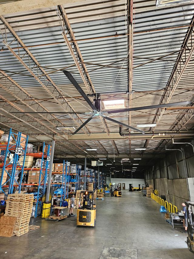 Warehouse aisle with stacked boxes, shelving, and a yellow forklift under a metal roof