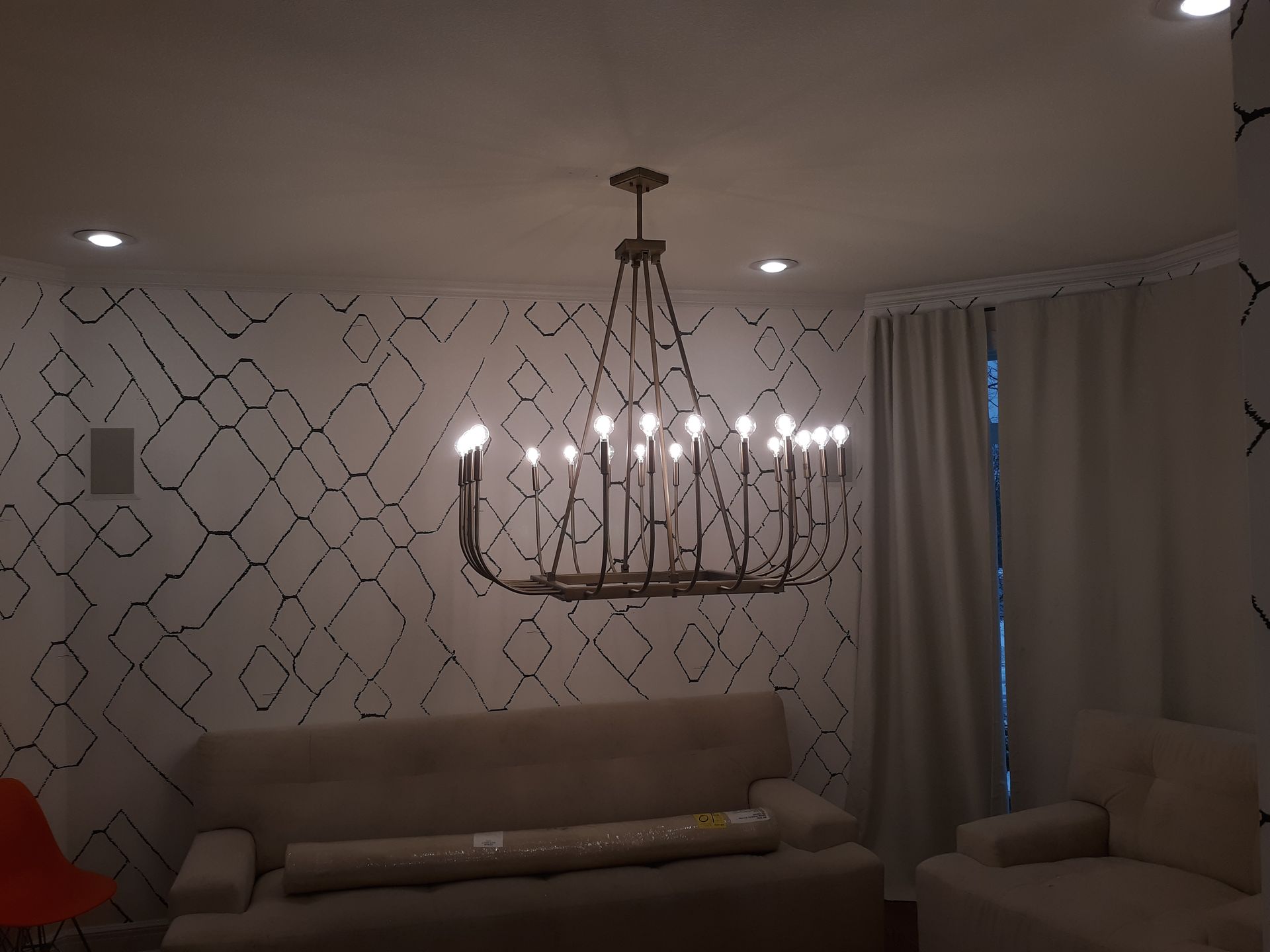 Living room with a beige sofa, ornate chandelier, patterned wallpaper, and curtains by a window