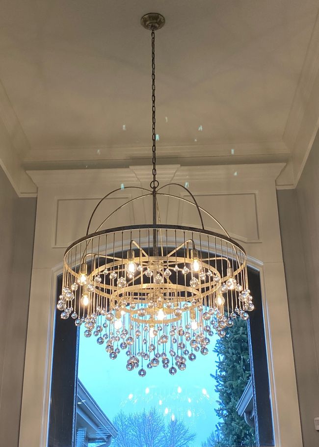 Ornate gold chandelier hanging from a ceiling above a bright window