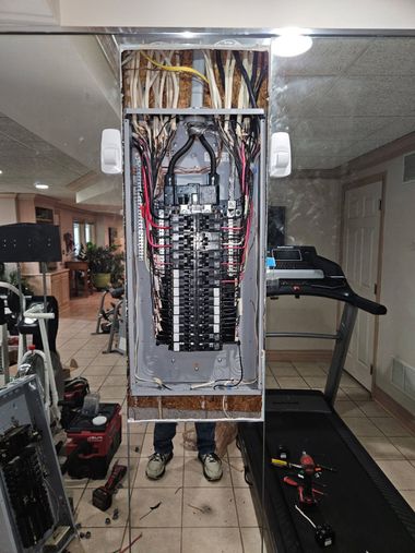 Open electrical panel with exposed wiring and breaker switches in a home interior.