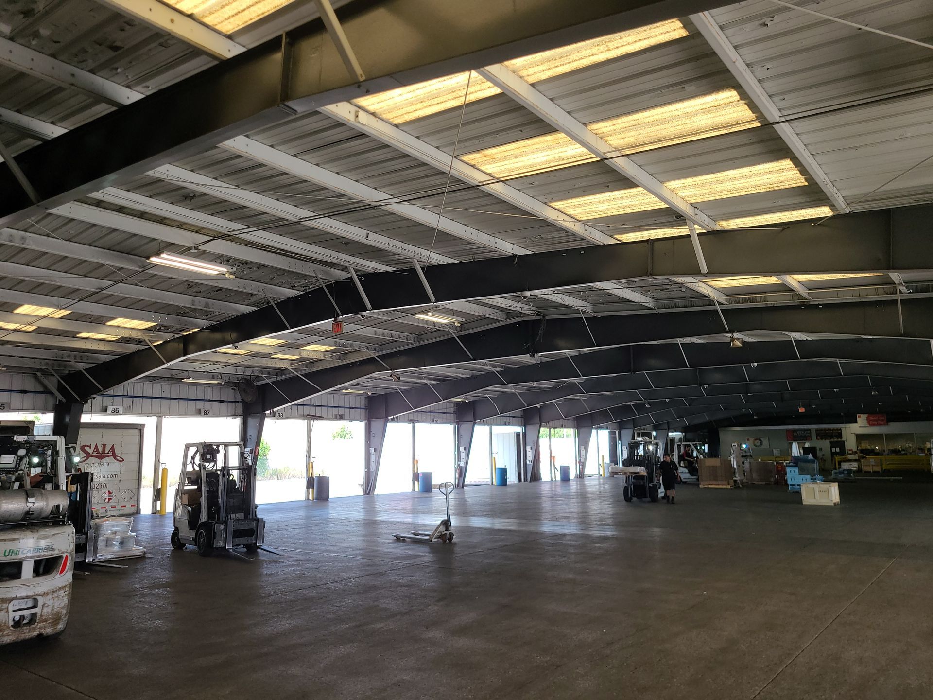 Inside a large warehouse with a forklift, open floor space, and bright light from doors at the far end.