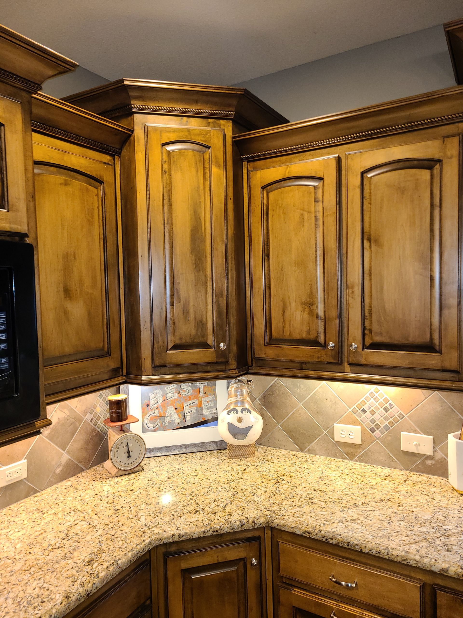 Wooden kitchen corner with upper cabinets, granite countertop, and decorative backsplash lighting.