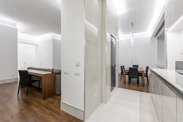 Modern apartment hallway and dining area with white walls, wood floors, and a table with chairs