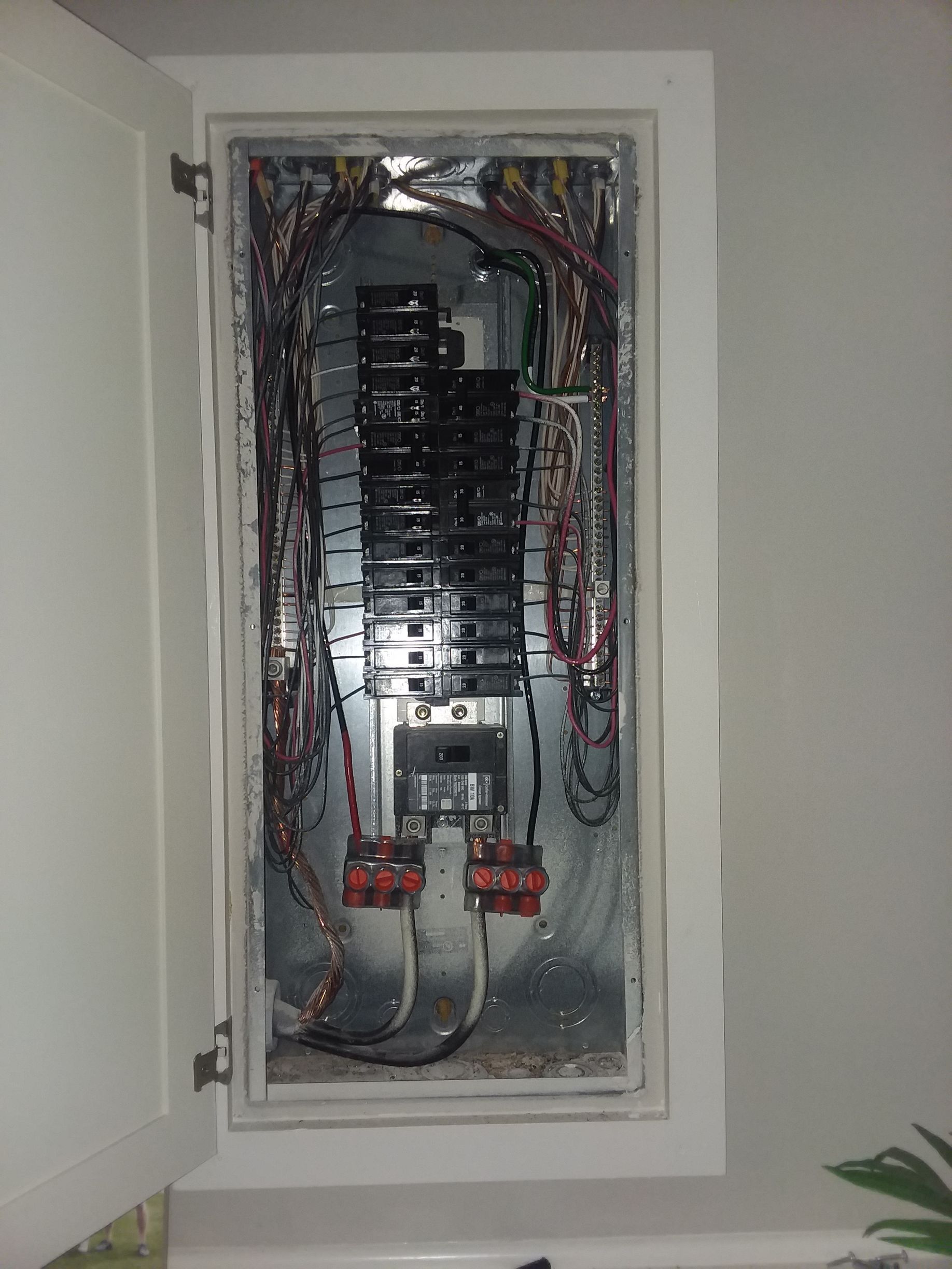 Open electrical breaker panel with exposed wiring inside a wall cabinet.