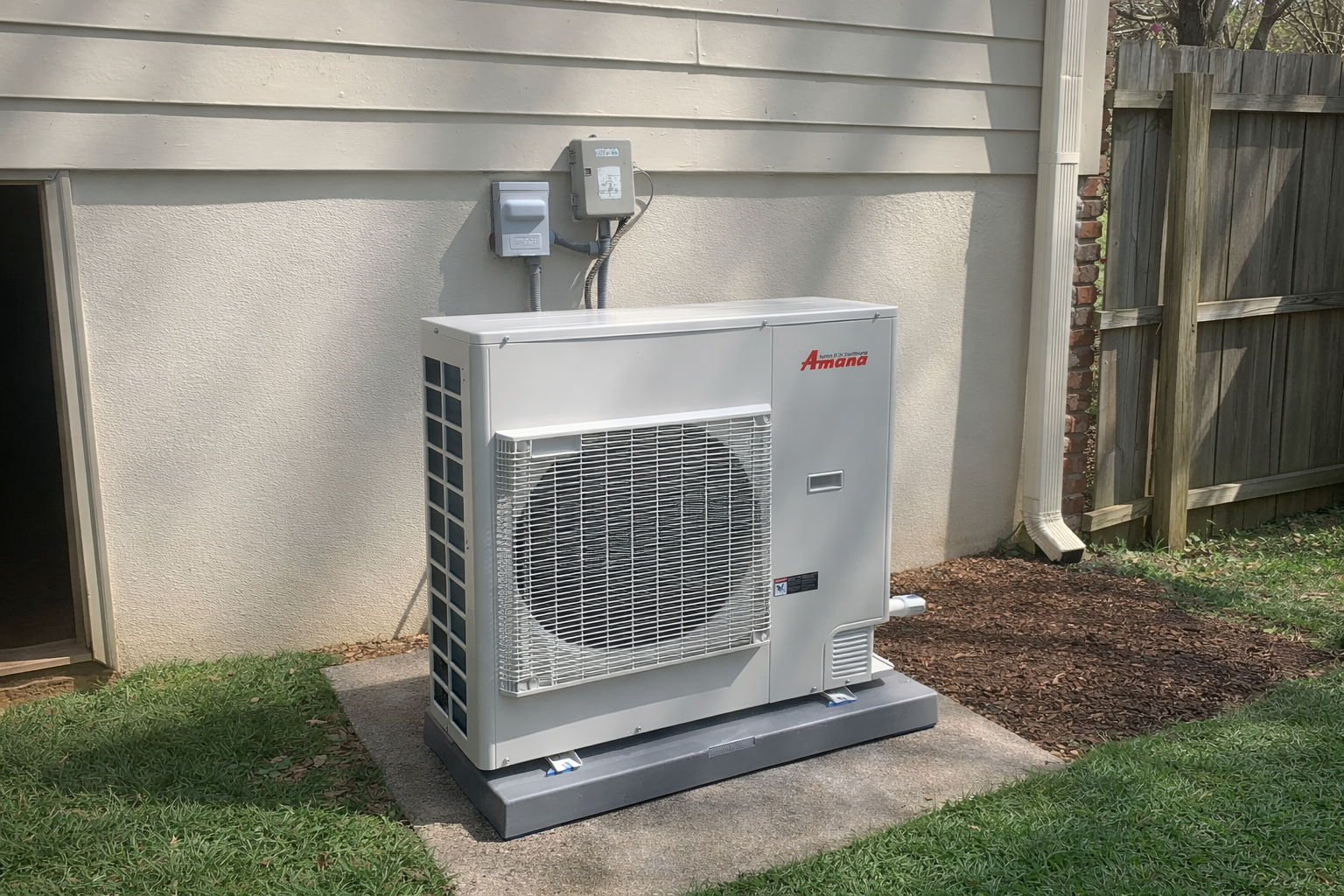 Single Amana HVAC unit outside of a customer's home in Hartwell GA with a fence, grass, and mulch next to the hvac unit