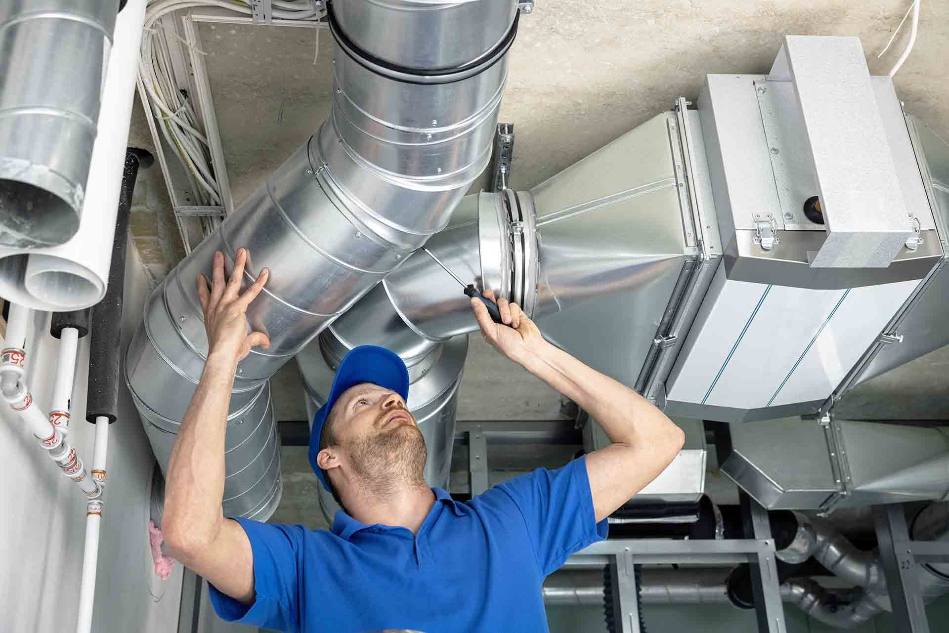 HVAC heating and cooling technician working on silver ducts in a customer's home in winder. HVAC tech wearing a blue uniform
