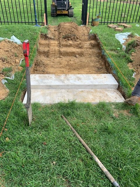 Construction site: concrete steps being built in a grassy yard, dirt path leading to a black gate.
