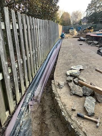 A trench dug along a wooden fence, with pipes and construction debris visible.