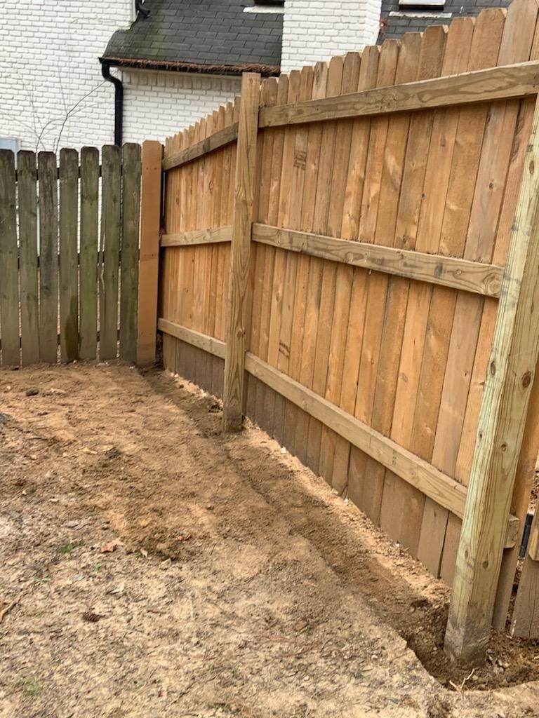 A wooden fence is sitting in the dirt in front of a house.