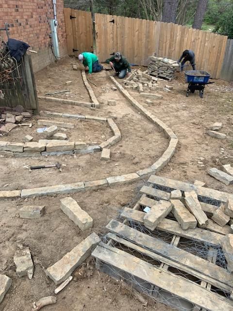A group of people are working on a brick walkway in a backyard.