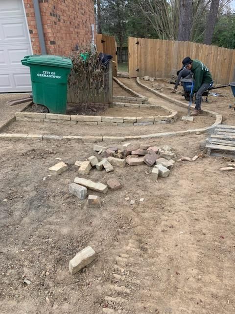 A person is building a stone path in a yard; scattered bricks are on the ground.