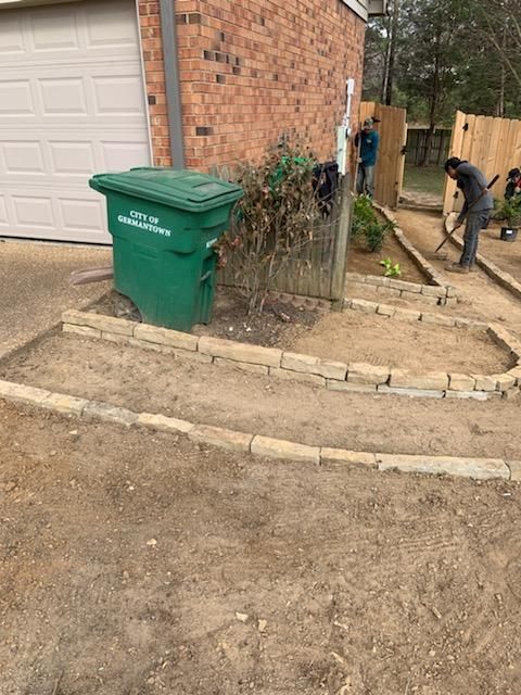 A green trash can is sitting in the dirt in front of a house.