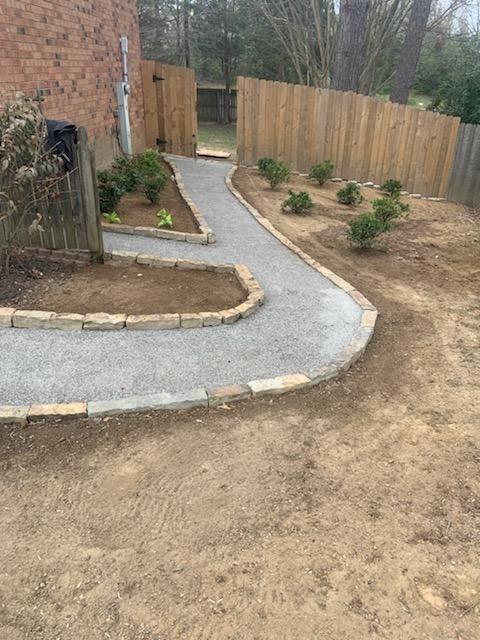 Stone path with brick borders in a backyard, leading to a wooden fence gate.