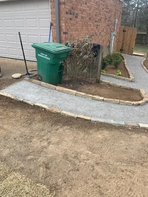 A green trash can is sitting on a sidewalk next to a garage door.