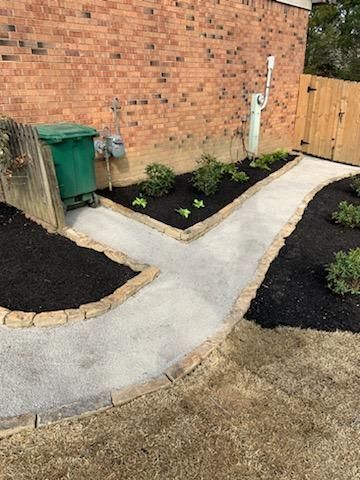 A concrete walkway leading to a garden next to a brick wall.